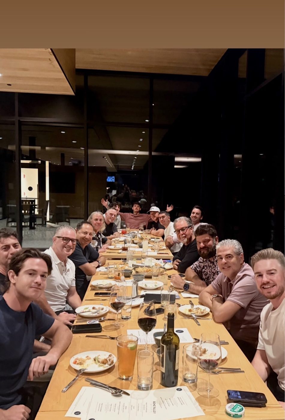 Members at one long dinner table, turning to smile at the camera.