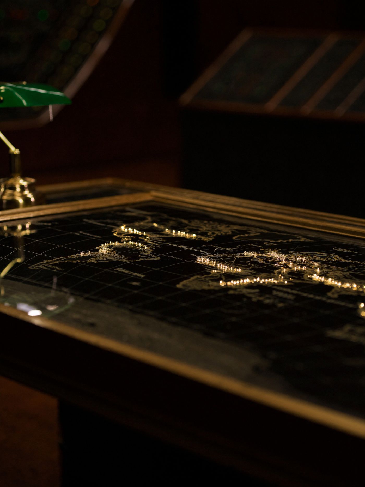 The control room's brass map table, gold marker lights glowing across the continents