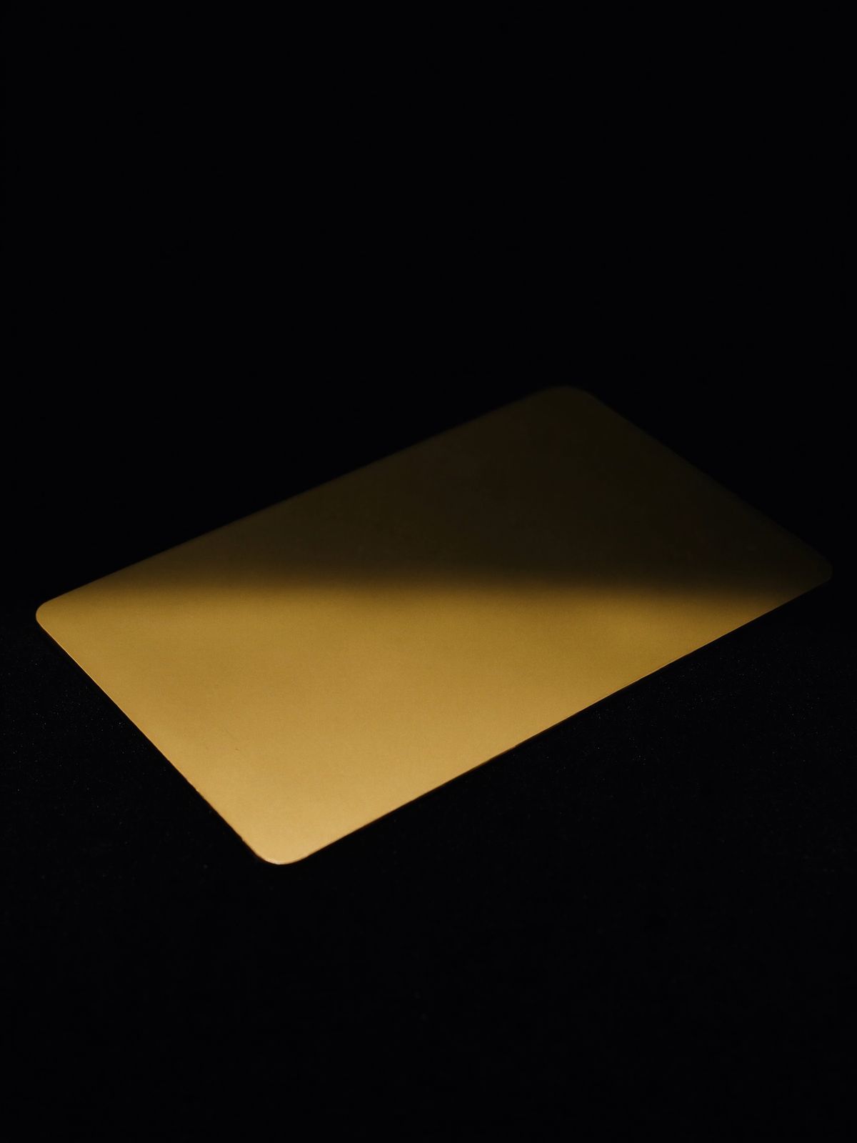 A blank card of solid brushed gold resting on black velvet under a single spotlight
