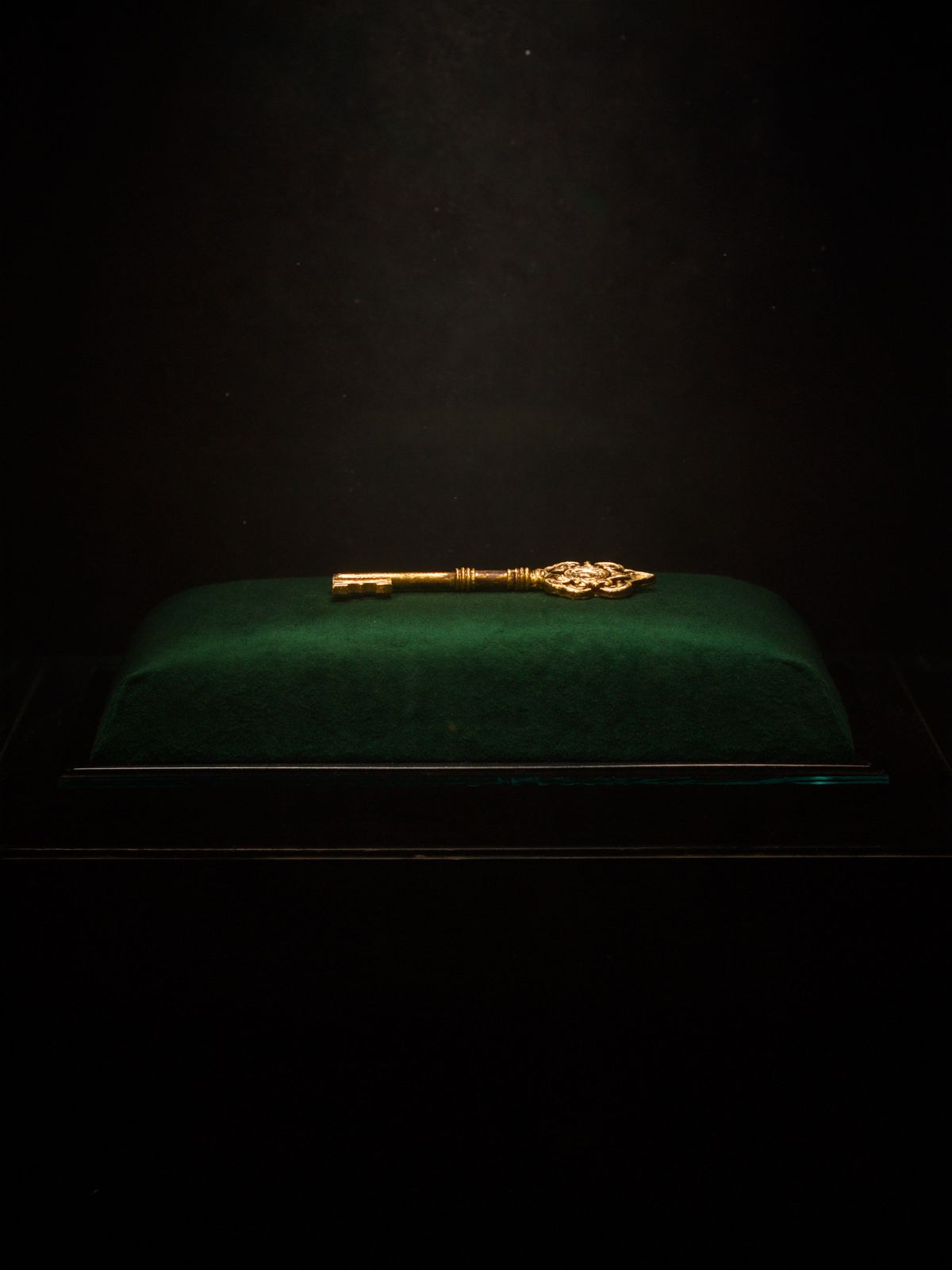 An ornate gold key resting on green velvet inside a glass case