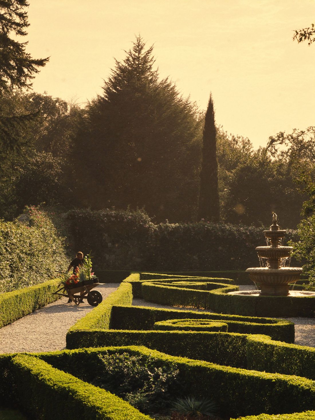 Formal estate gardens and a stone fountain flanking the lane at golden hour