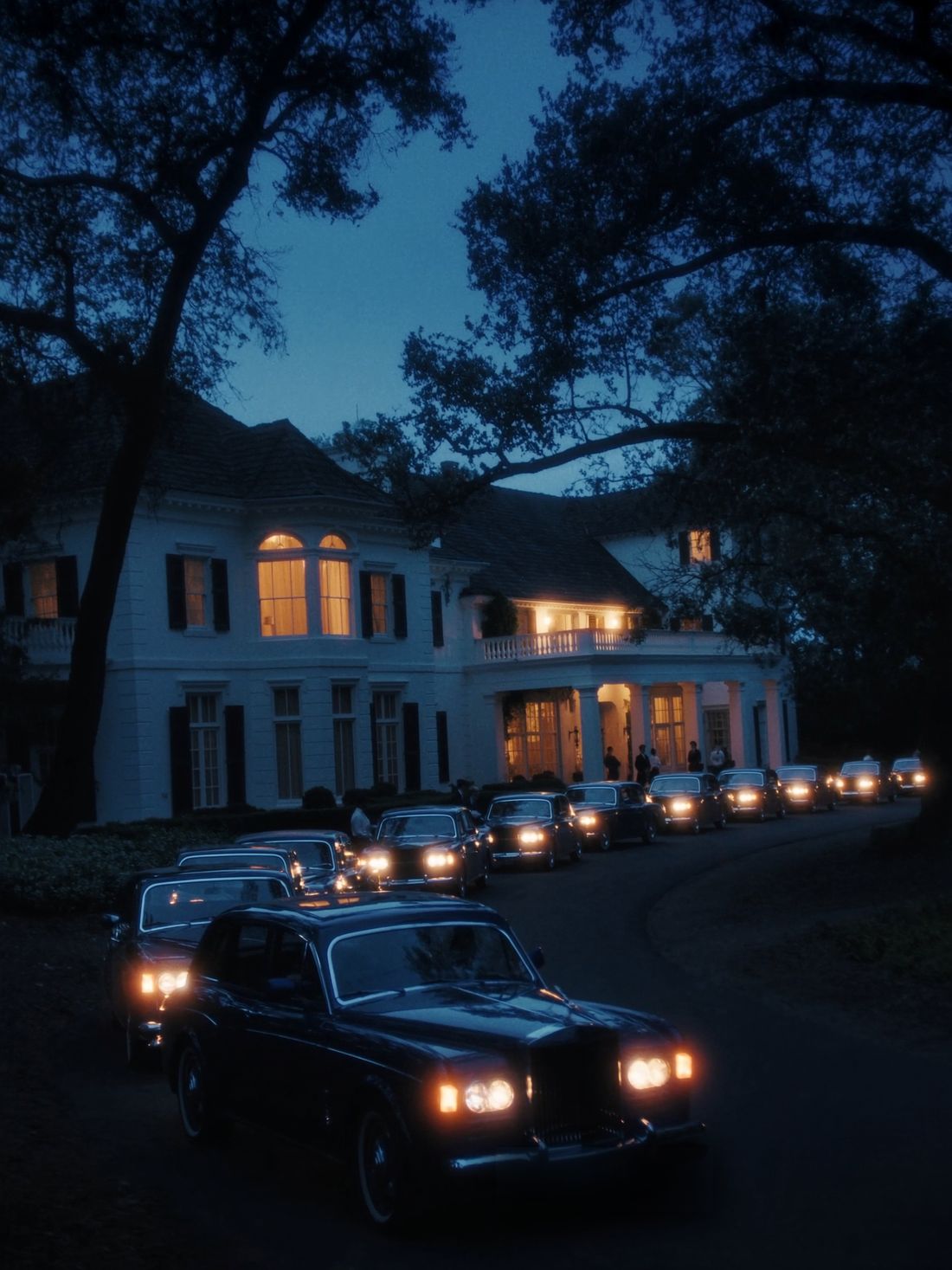 The estate at blue hour, every window lit, cars arriving up the drive