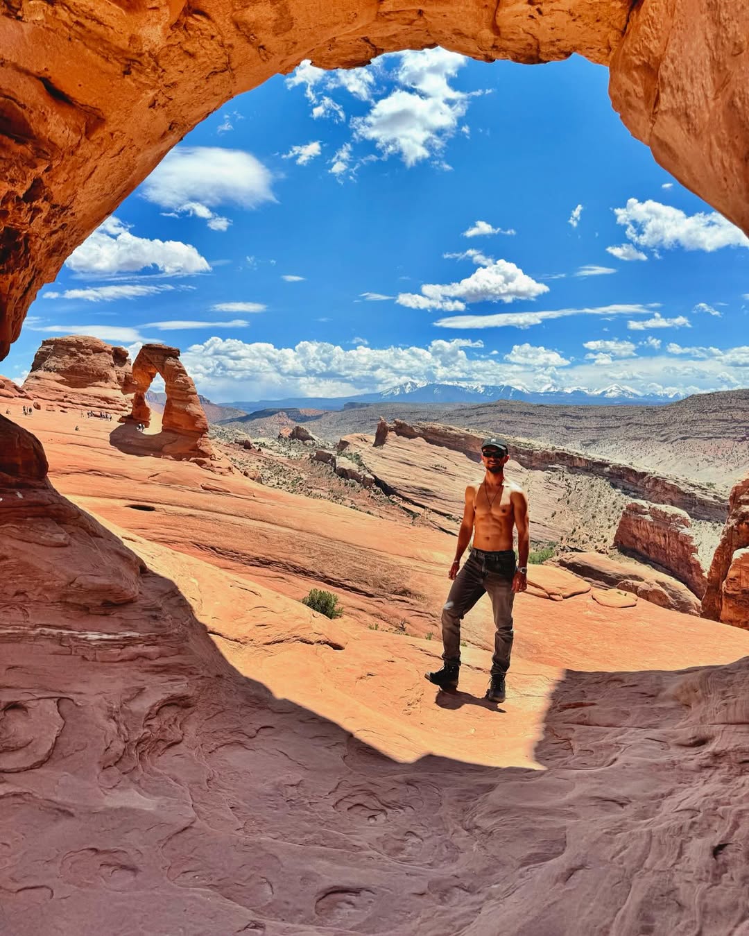 David Mata enmarcado por un arco de piedra con el Delicate Arch al fondo, en Utah