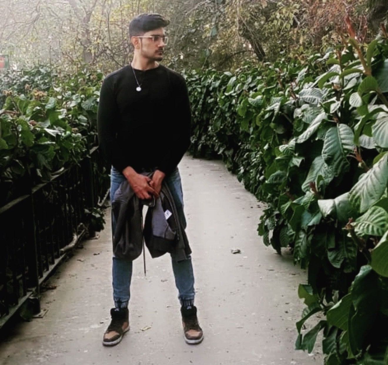 Muhammad Fahad standing on a garden path, wearing a black cap, glasses and a black sweater
