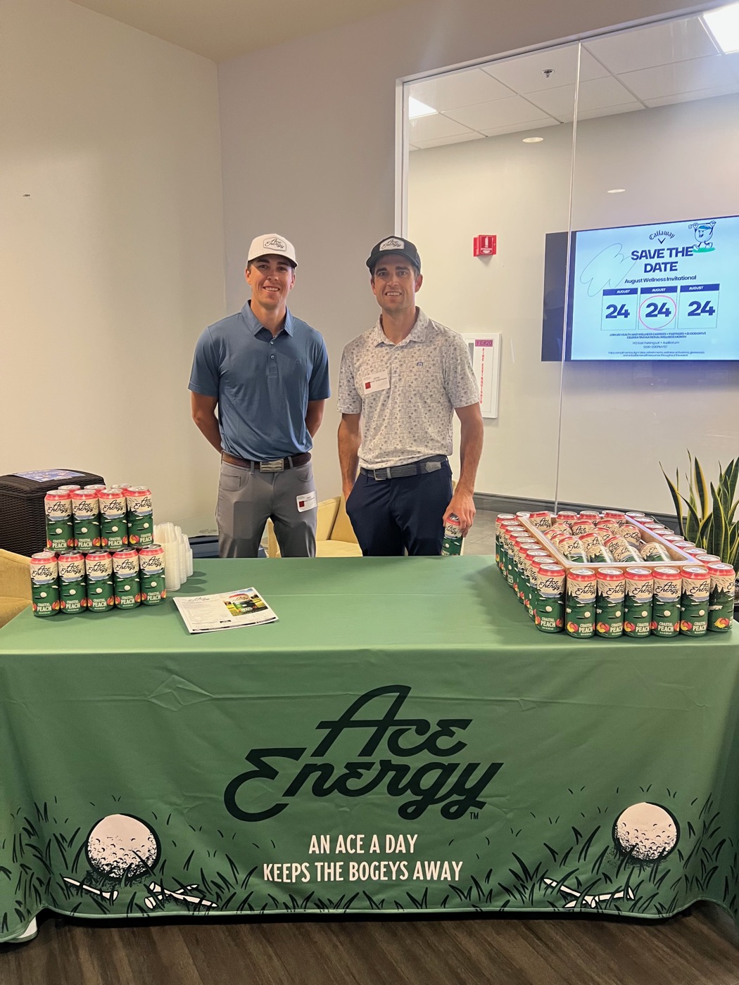 Tommy and Trevor Soderholm at an Ace Energy activation booth, stocked with Coastal Peach cans under the brand's An Ace a Day Keeps the Bogeys Away tablecloth.