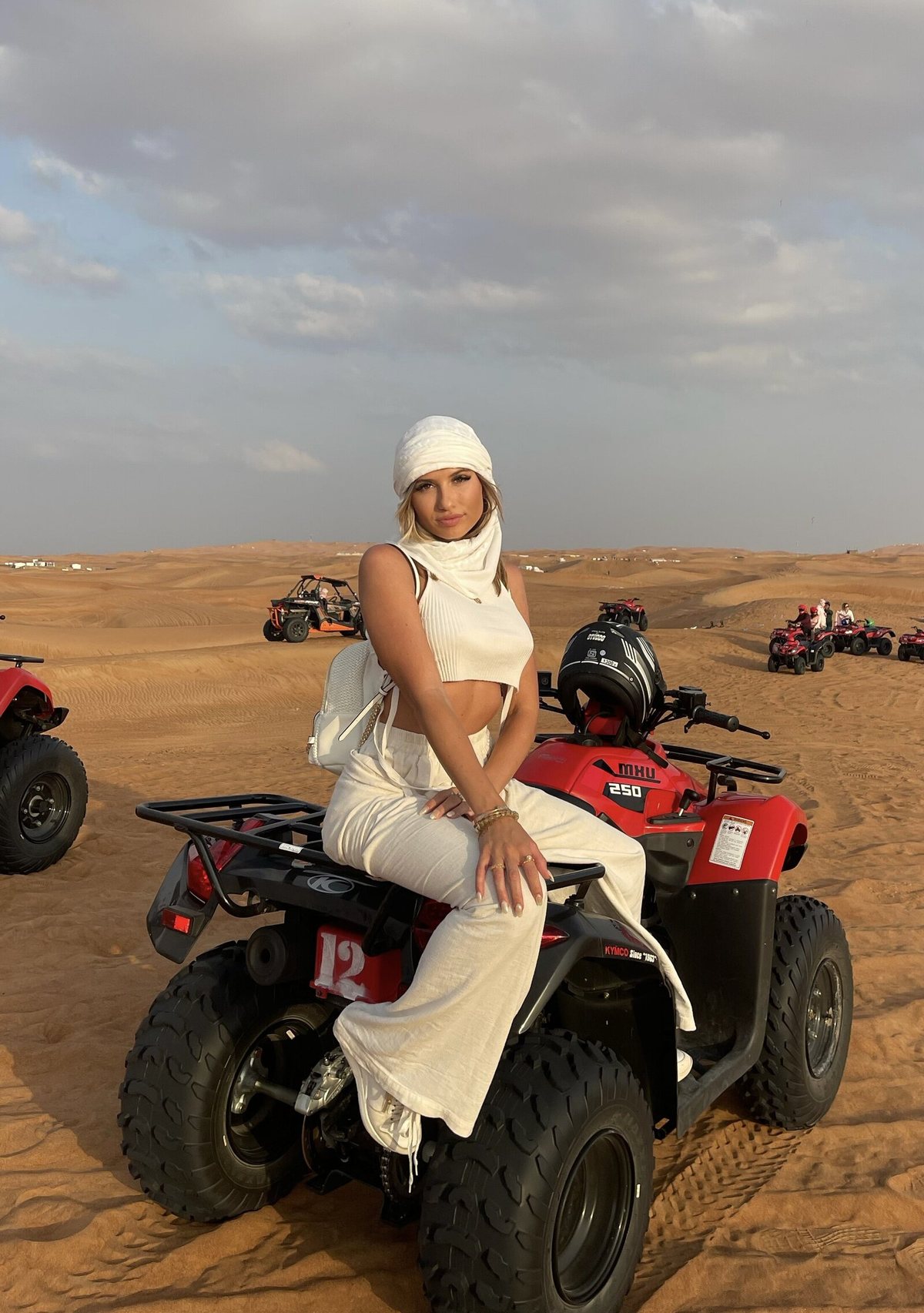 Zianna Marie seated on a quad bike in the desert dunes, dressed in white
