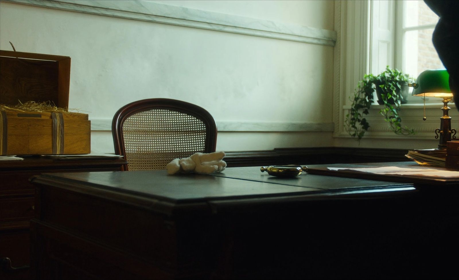The curator's receiving desk — white cotton gloves, a brass magnifying glass, a green banker's lamp, and an open packing crate beside the desk