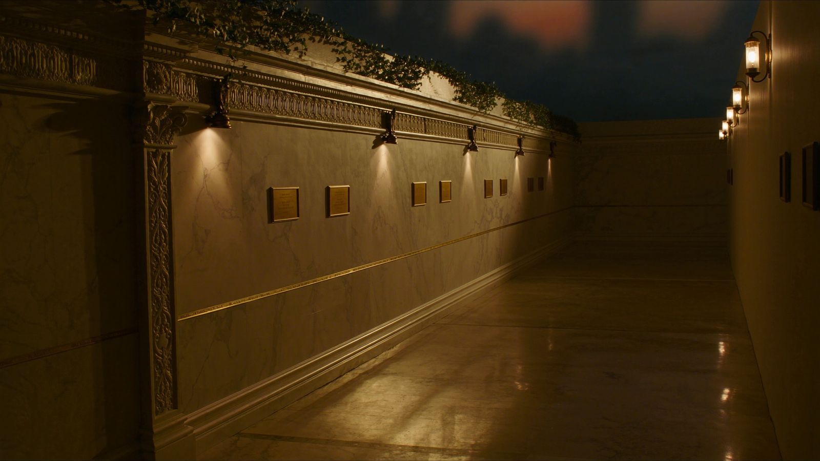 The museum's marble corridor — brass picture lights, blank brass plates, ivy along the cornice, and a single engraved gold line running the length of the wall