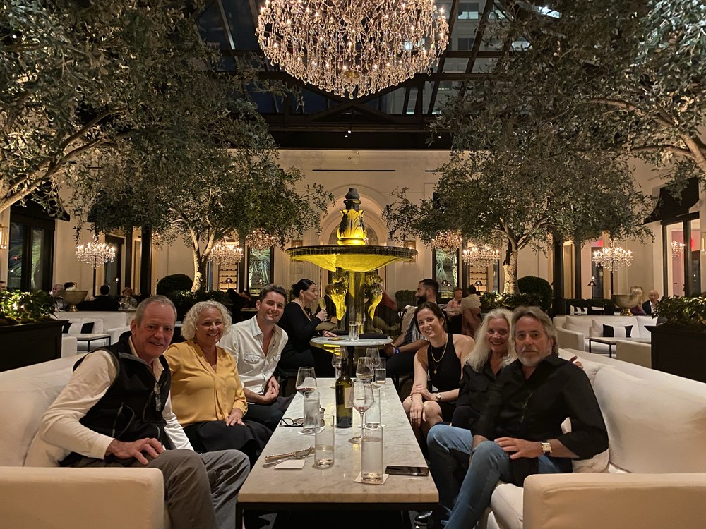Six members around one table at dinner, under a chandelier.
