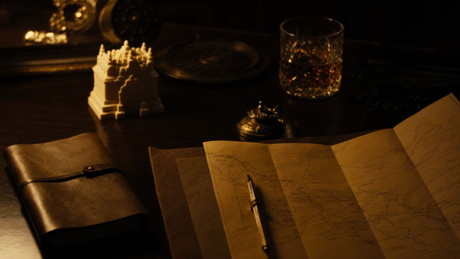 The founder's desk — field journal, brass compass, expedition map, and a carved temple fragment in candlelight