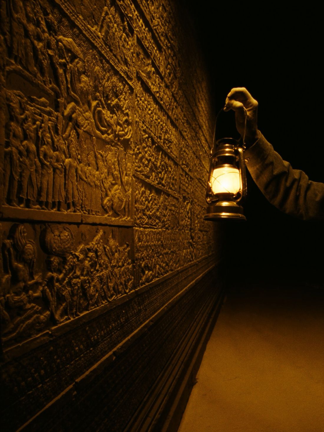 A lantern held up to a carved gallery wall of figures and stories