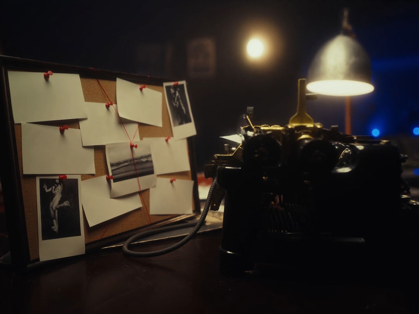 A vintage typewriter under a warm lamp beside a small cork board pinned with blank cards, red pins and red string