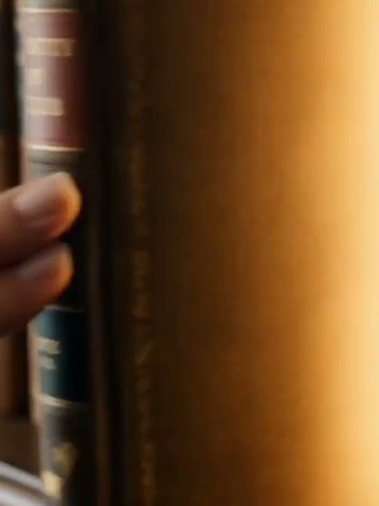 A hand drawing one leather-bound book off the shelf, warm gold light spilling out of the gap it leaves