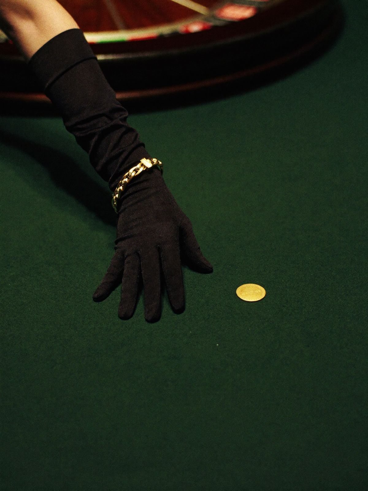 A hand in a long black satin glove placing a single gold marker on deep green felt