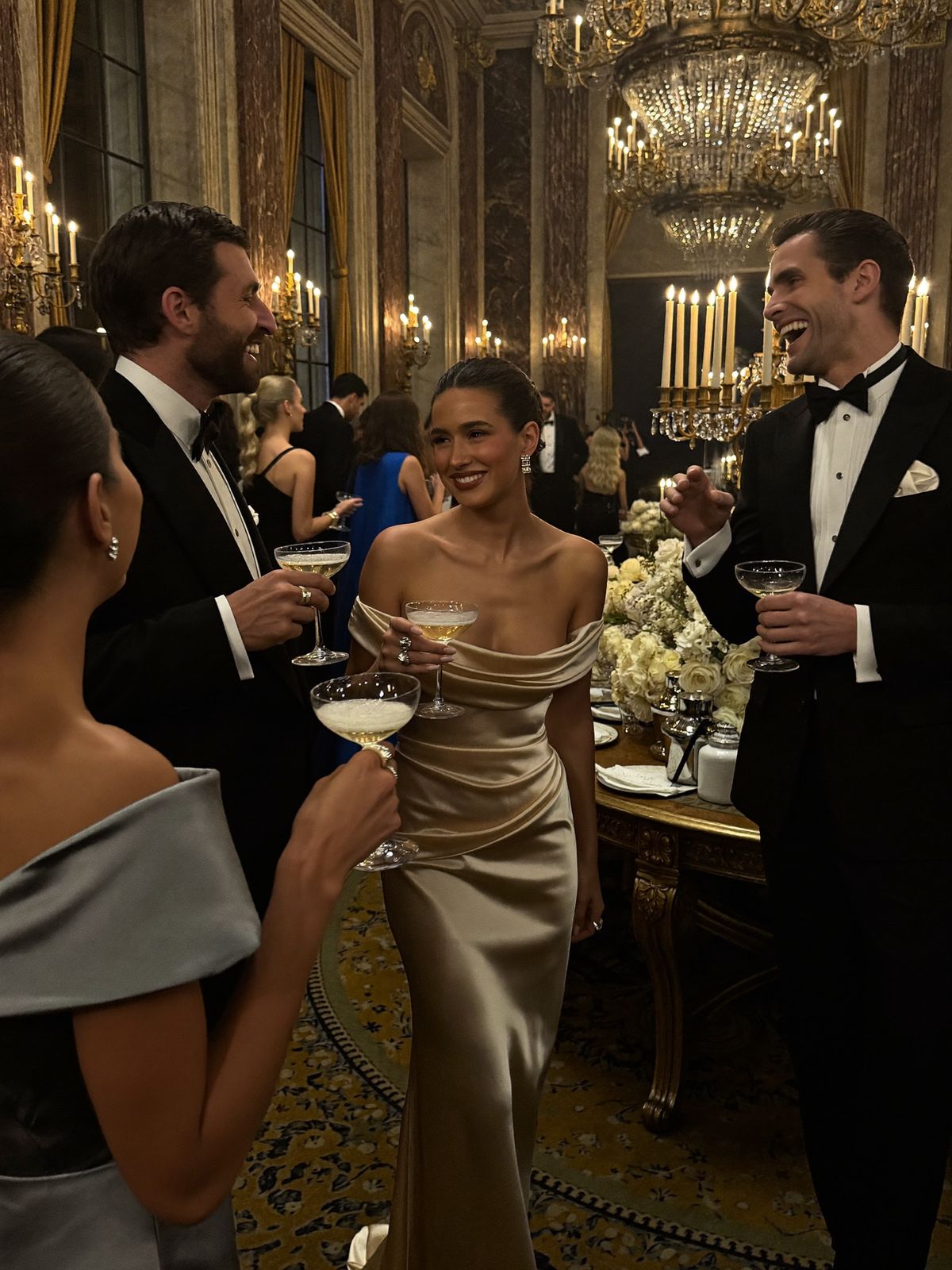 A black-tie soirée under crystal chandeliers — gowns, tuxedos and champagne coupes in a gilded salon