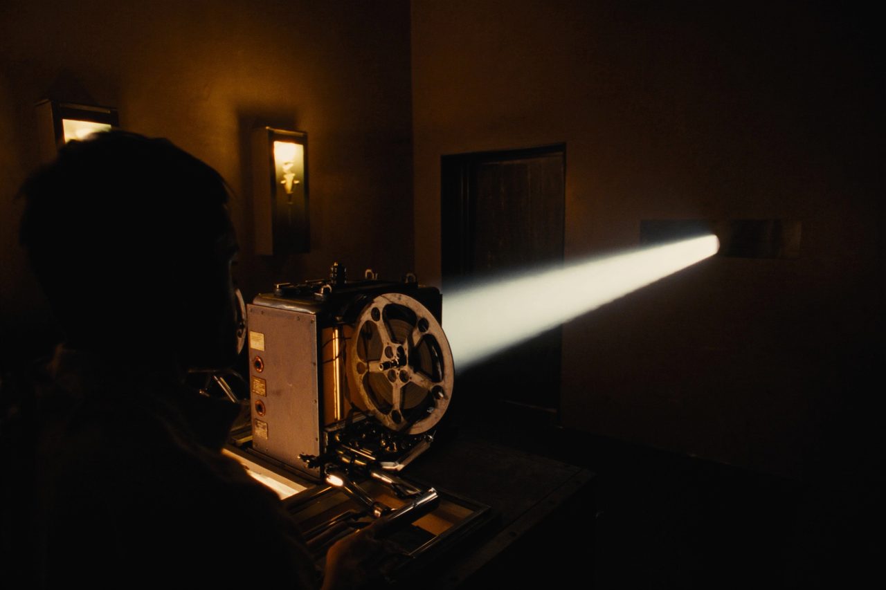 A 35mm film projector running in a dark booth, its beam cutting out through the port window