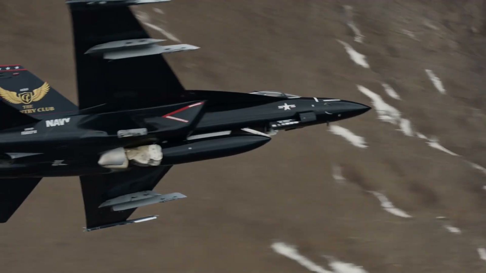 A black fighter jet wearing The Country Club crest banking through the mountains