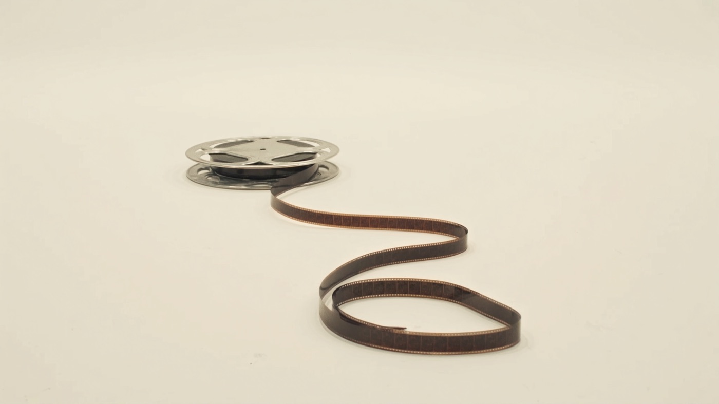 A silver film reel unspooling a ribbon of film across the white room floor