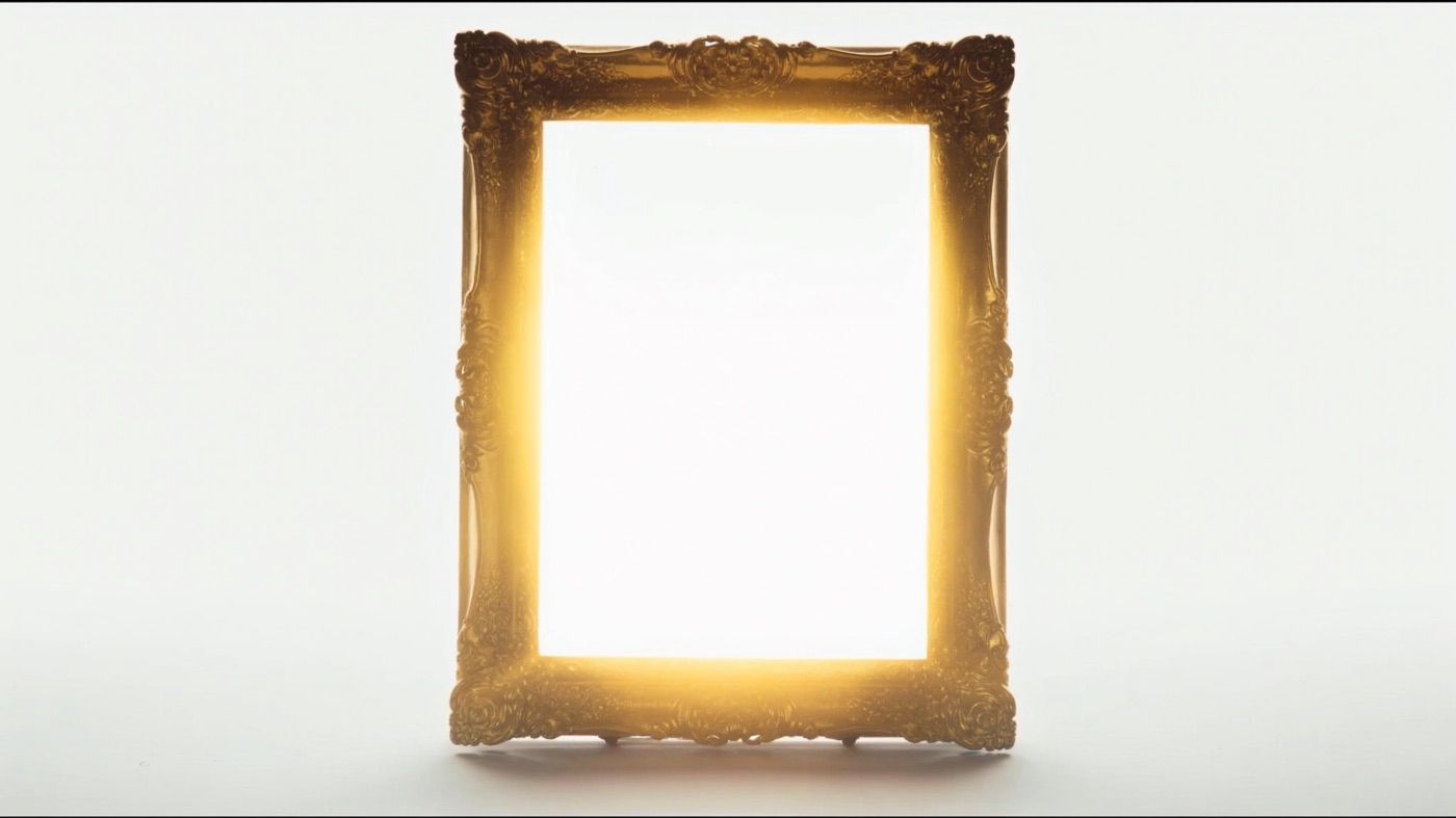 An empty gilded frame standing in the white room with golden light pouring through it, waiting for a portrait