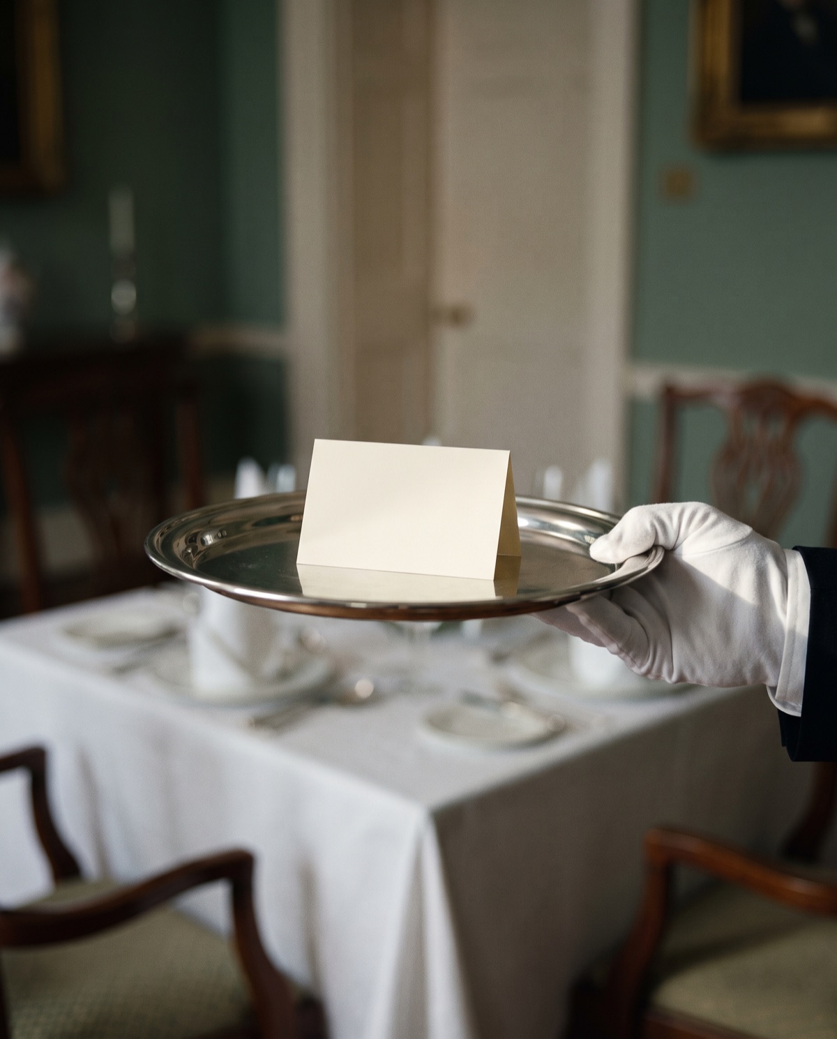 A calling card presented on a butler's silver tray in candlelight